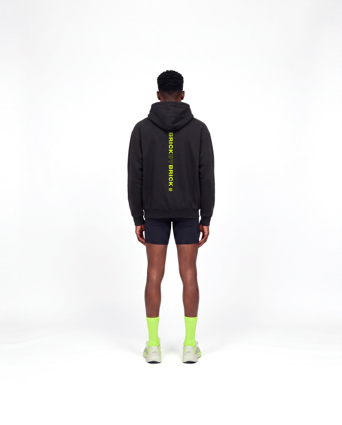 Model wearing the Brick by Brick oversize hoodie in black — back view with BRICK BY BRICK set vertically down the centre in lime green — Ansicht 4