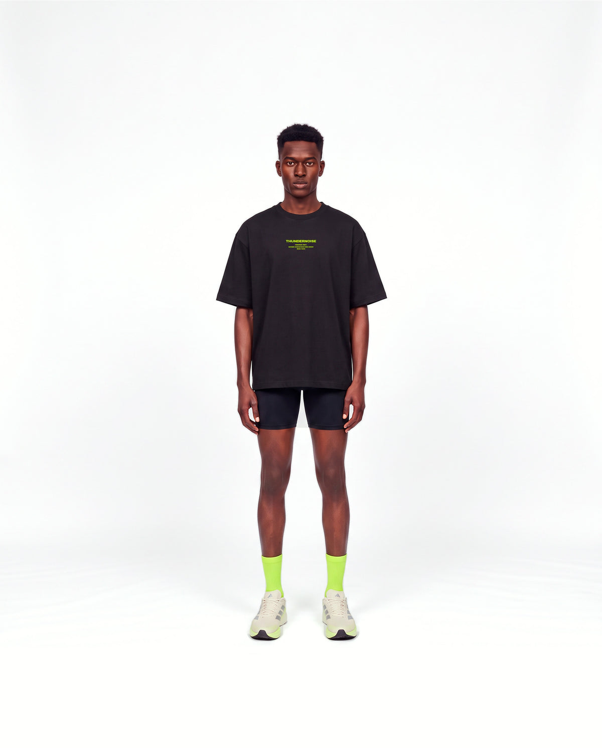 Model wearing the Brick by Brick oversize t-shirt in black — front view with the THUNDERNOISE TRAINING DEPT block centred on the chest in lime green — Vista 2