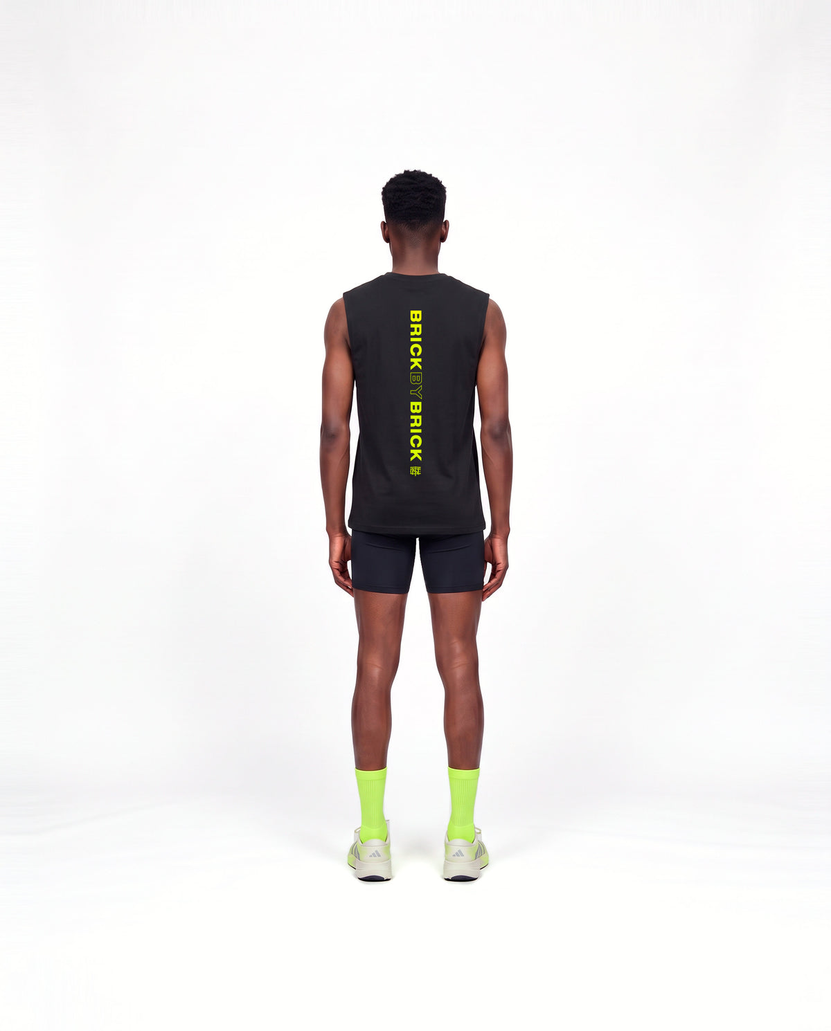 Model wearing the Brick by Brick tank top in black — back view with BRICK BY BRICK set vertically down the centre in lime green — Vista 4