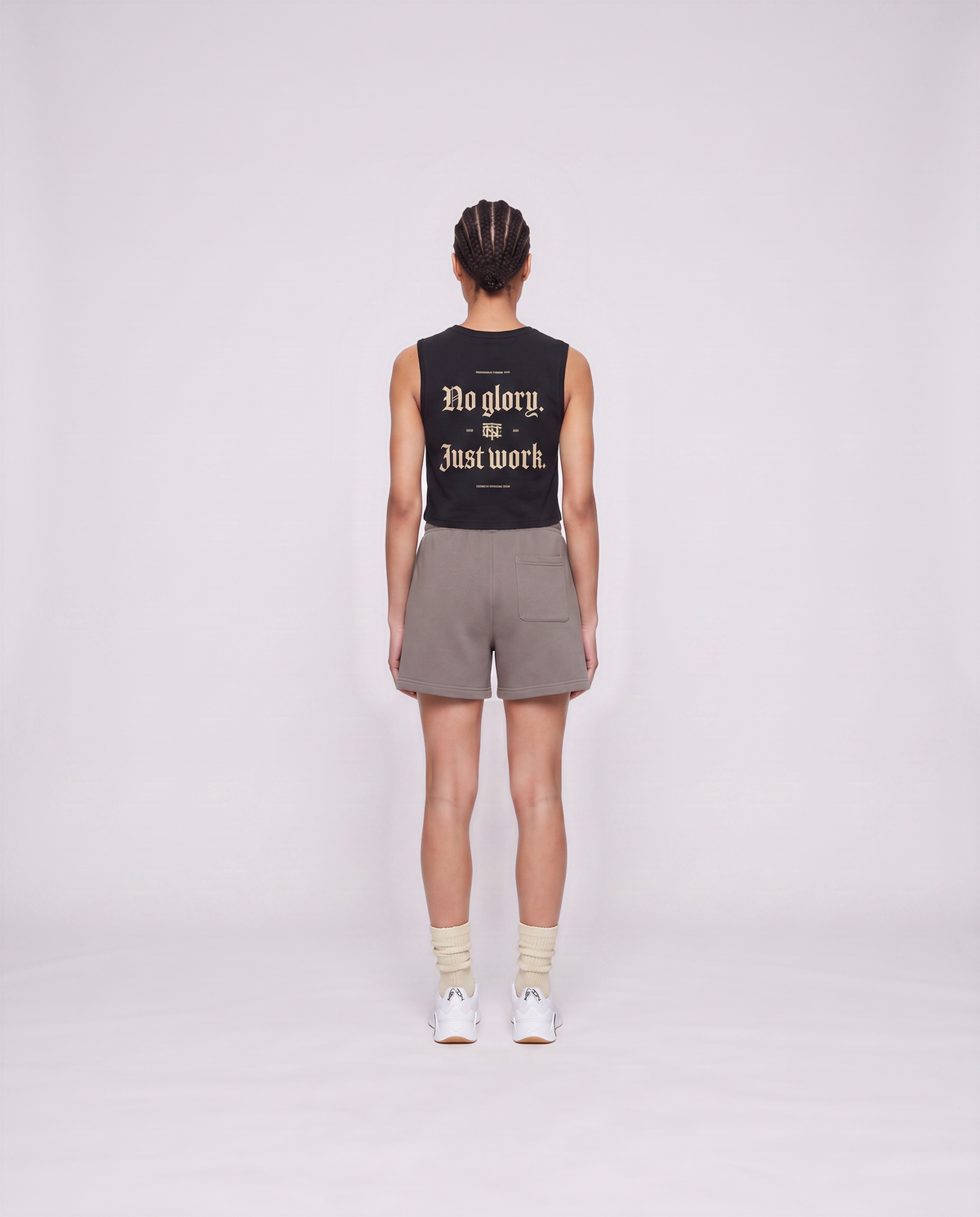 Model wearing the No Glory Just Work cropped tank top in black — back view with the NO GLORY JUST WORK blackletter print in sand with the Thundernoise monogram — Vue 4