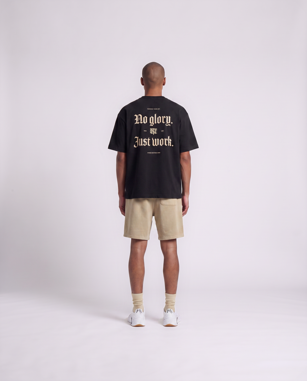 Model wearing the No Glory Just Work oversize t-shirt in black — back view with the NO GLORY JUST WORK blackletter print in sand with the Thundernoise monogram — Ansicht 4