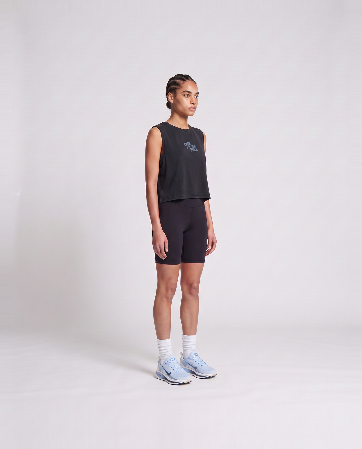 Model wearing the One More Mile cropped tank top in black — three-quarter view showing the cropped fit — Vista 3