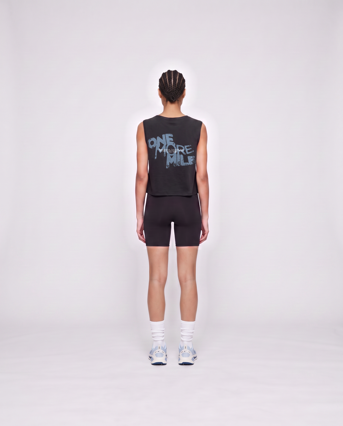 Model wearing the One More Mile cropped tank top in black — back view with the dripping ONE MORE MILE graffiti print in slate blue — Vista 4
