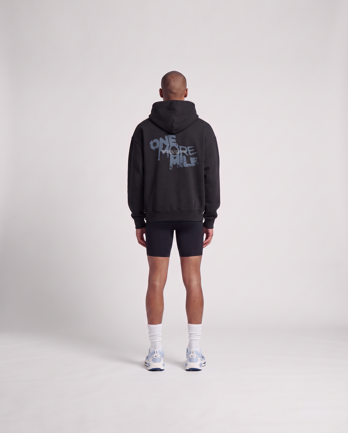 Model wearing the One More Mile oversize hoodie in black — back view with the dripping ONE MORE MILE graffiti print in slate blue — Vista 4