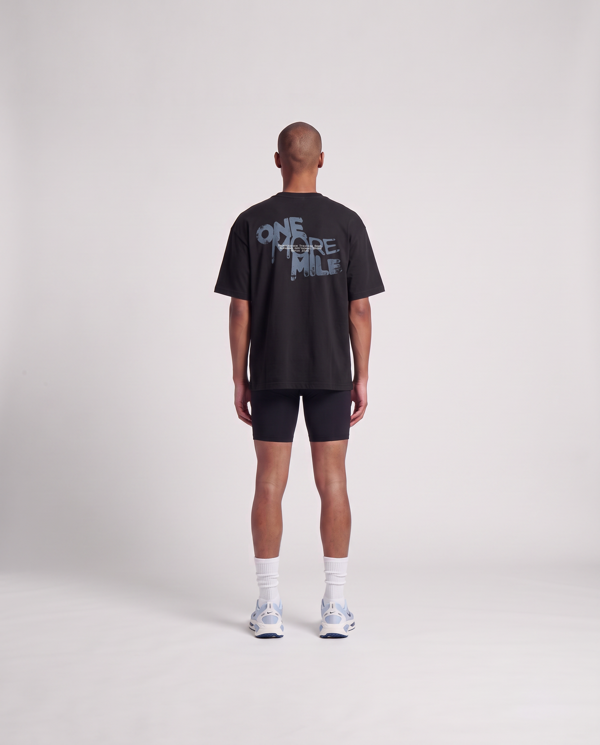 Model wearing the One More Mile oversize t-shirt in black — back view with the dripping ONE MORE MILE graffiti print in slate blue — Vista 4