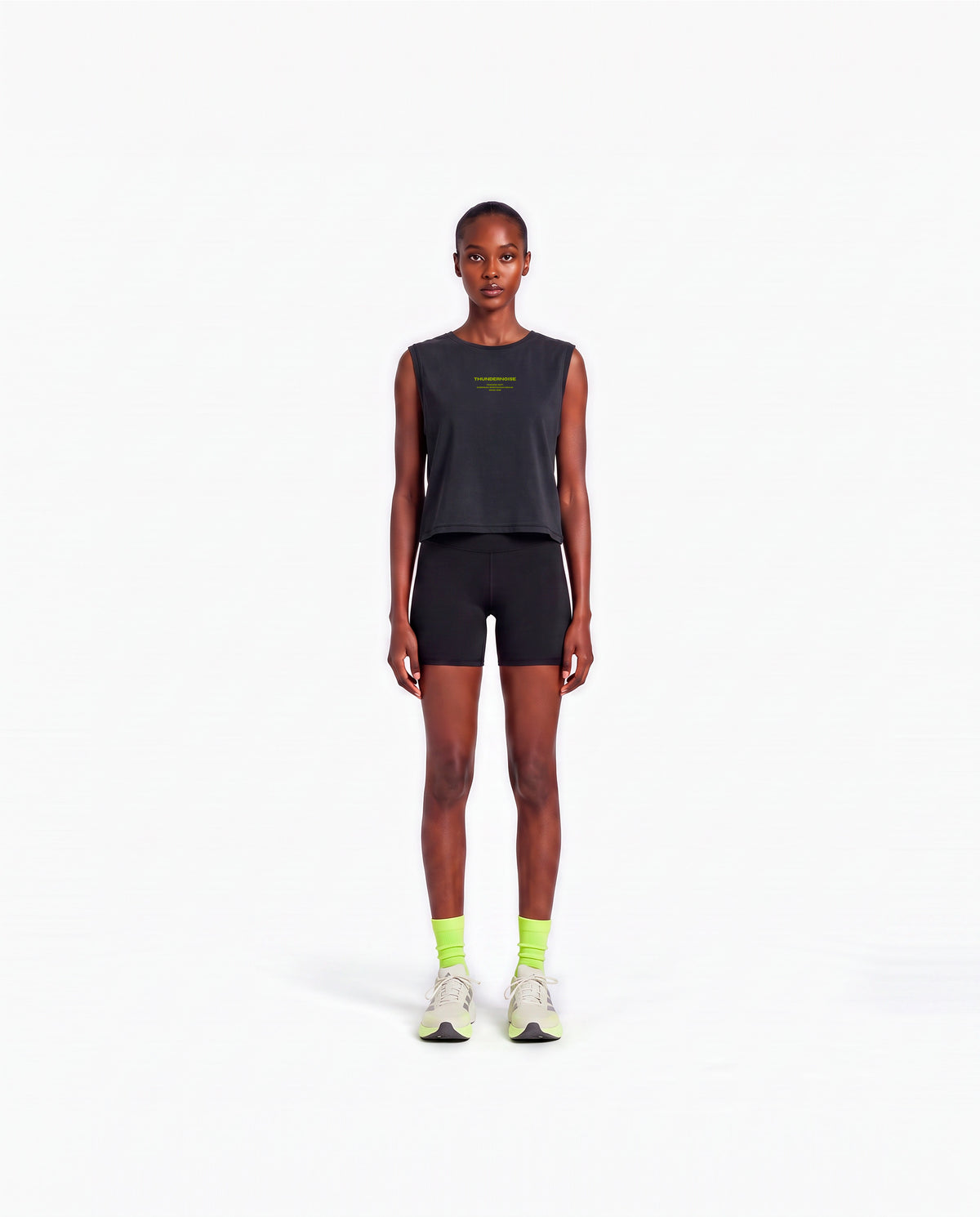 Model wearing the Brick by Brick cropped tank top in black — front view with the THUNDERNOISE TRAINING DEPT block centred on the chest in lime green — Vista 2
