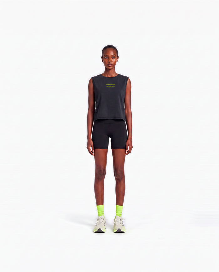 Model wearing the Brick by Brick cropped tank top in black — front view with the THUNDERNOISE TRAINING DEPT block centred on the chest in lime green