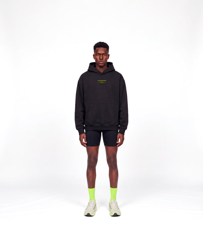 Model wearing the Brick by Brick oversize hoodie in black — front view with the THUNDERNOISE TRAINING DEPT block centred on the chest in lime green