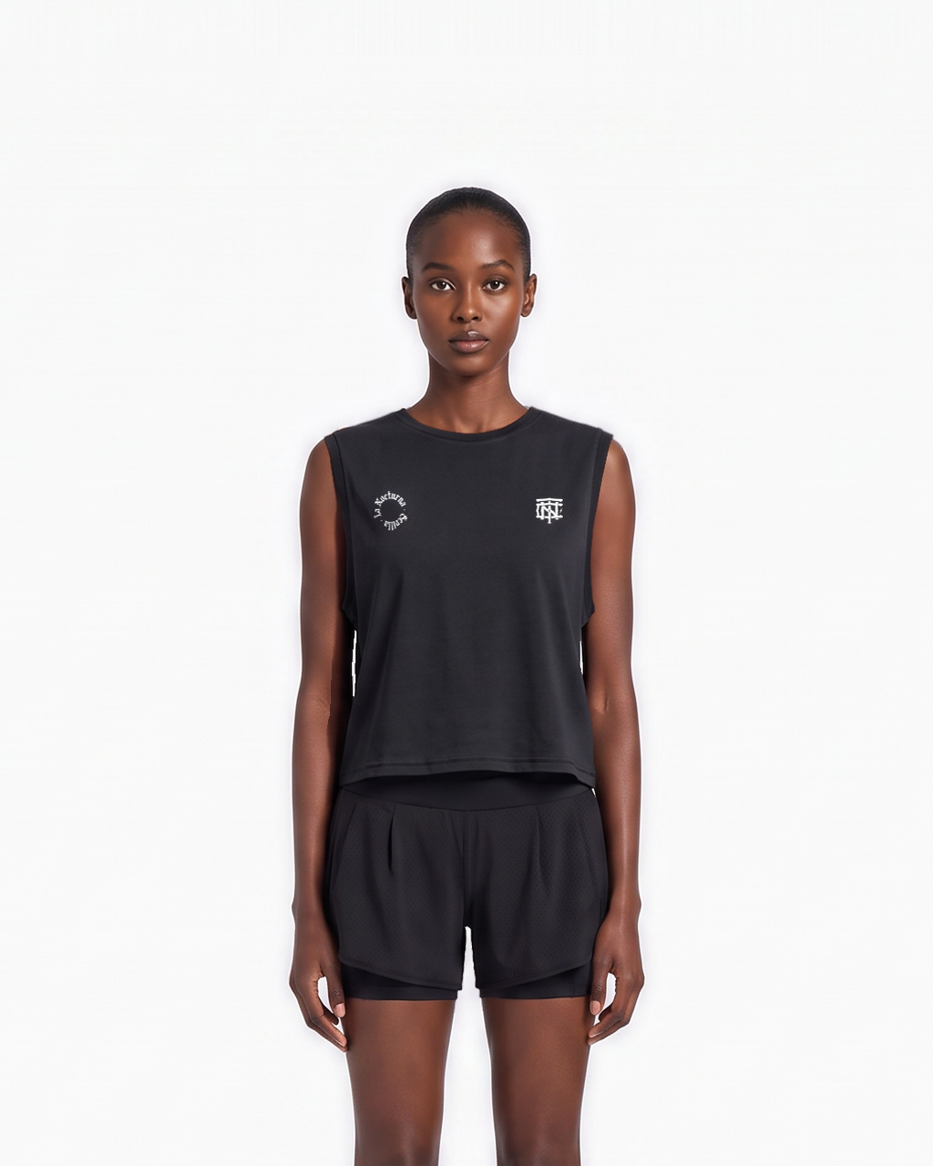 Model wearing the Let's Run the Night cropped tank top in black — front view, close crop on the La Nocturna Sevilla seal and the TN monogram in white — Ansicht 3
