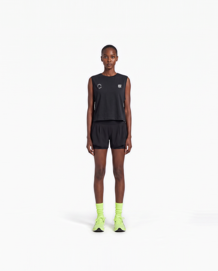 Model wearing the Let's Run the Night cropped tank top in black — front view with the La Nocturna Sevilla seal and the TN monogram in white