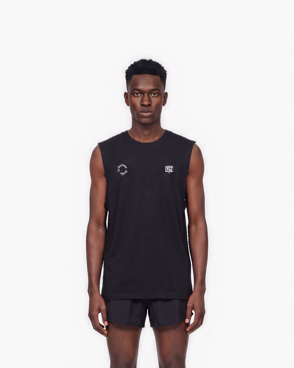 Model wearing the Let's Run the Night tank top in black — front view, close crop on the La Nocturna Sevilla seal and the TN monogram in white — Vista 3
