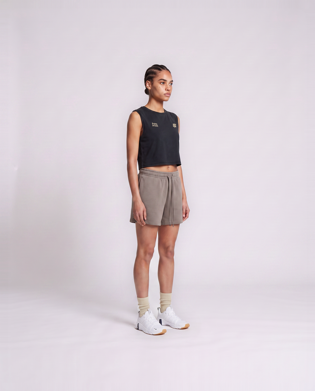 Model wearing the No Glory Just Work cropped tank top in black — three-quarter view showing the cropped fit — Vue 3
