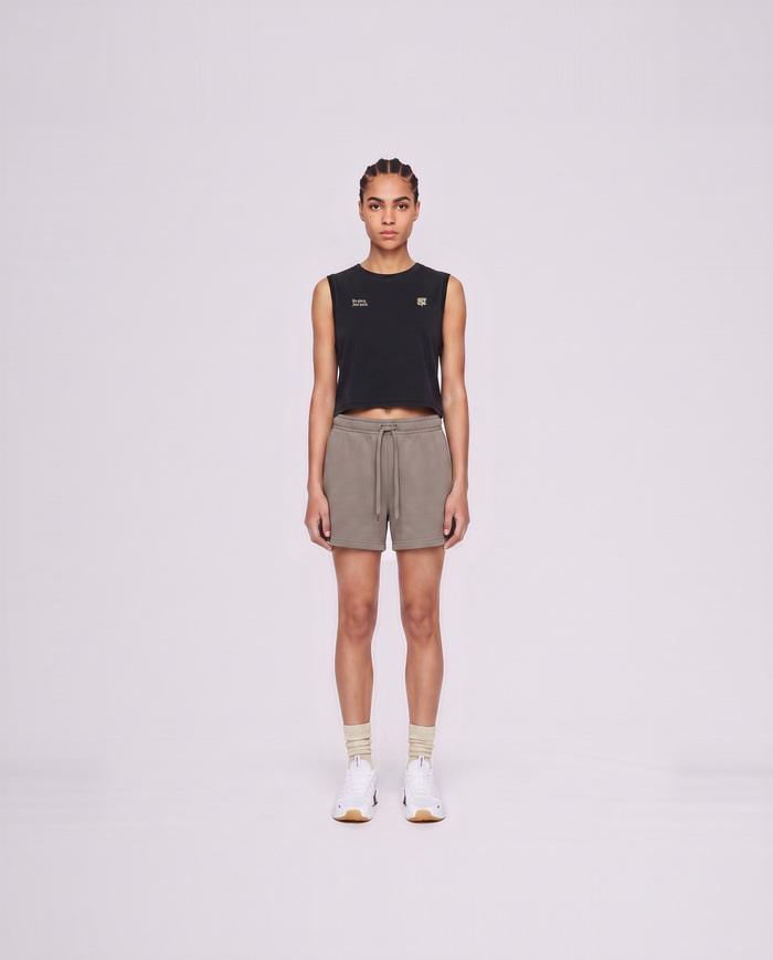 Model wearing the No Glory Just Work cropped tank top in black — front view with the left-chest NO GLORY JUST WORK wordmark and the right-chest Thundernoise monogram in sand