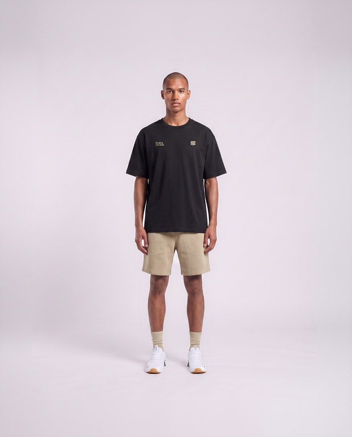 Model wearing the No Glory Just Work oversize t-shirt in black — front view with the left-chest NO GLORY JUST WORK wordmark and the right-chest Thundernoise monogram in sand