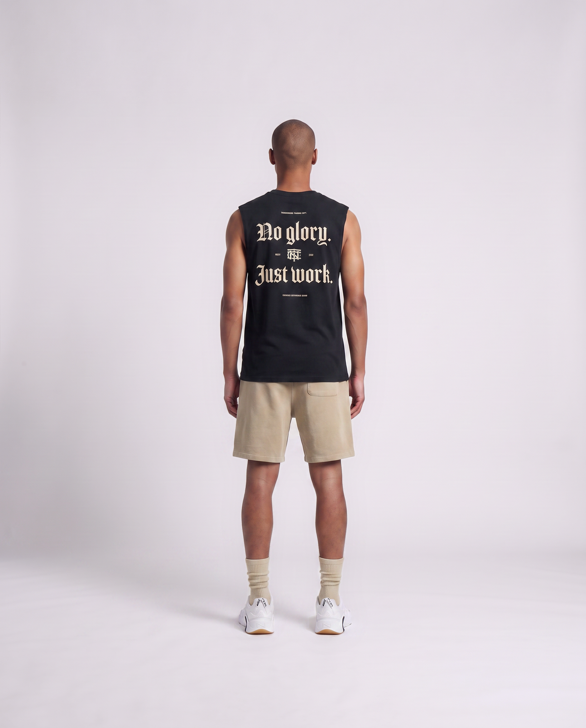 Model wearing the No Glory Just Work tank top in black — back view with the NO GLORY JUST WORK blackletter print in sand with the Thundernoise monogram — Ansicht 4
