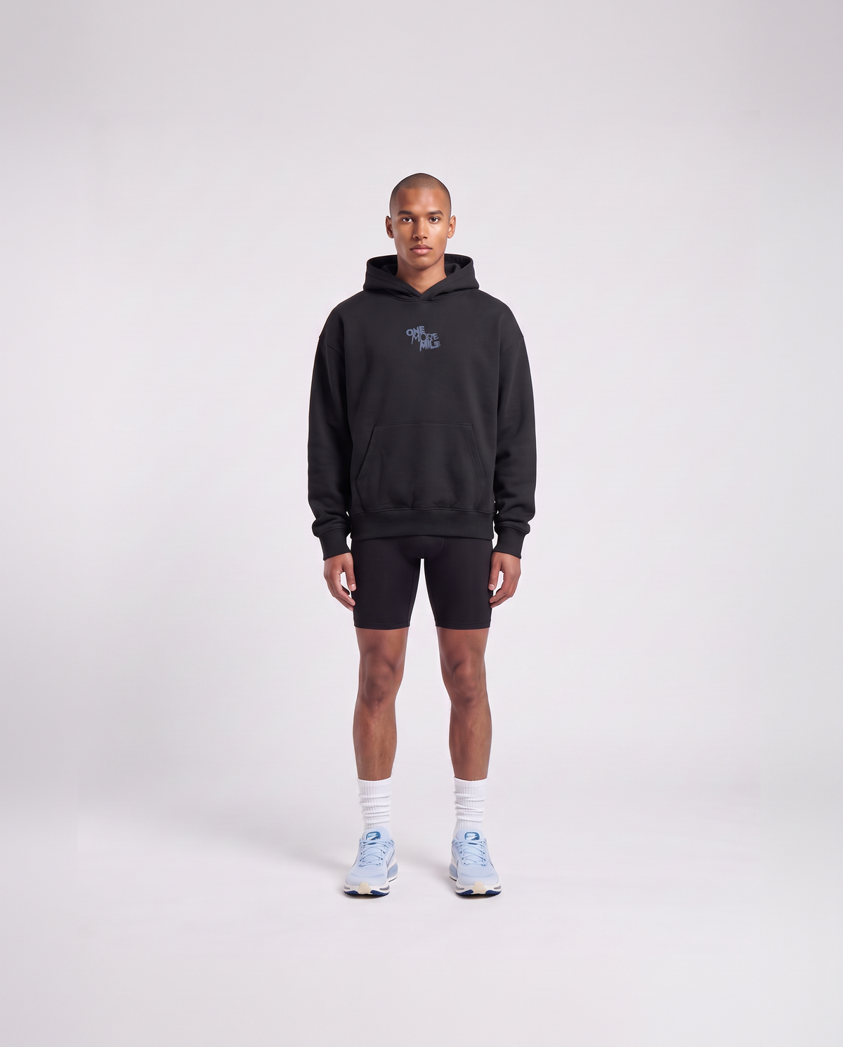 Model wearing the One More Mile oversize hoodie in black — front view with the ONE MORE MILE graffiti mark at the chest in slate blue