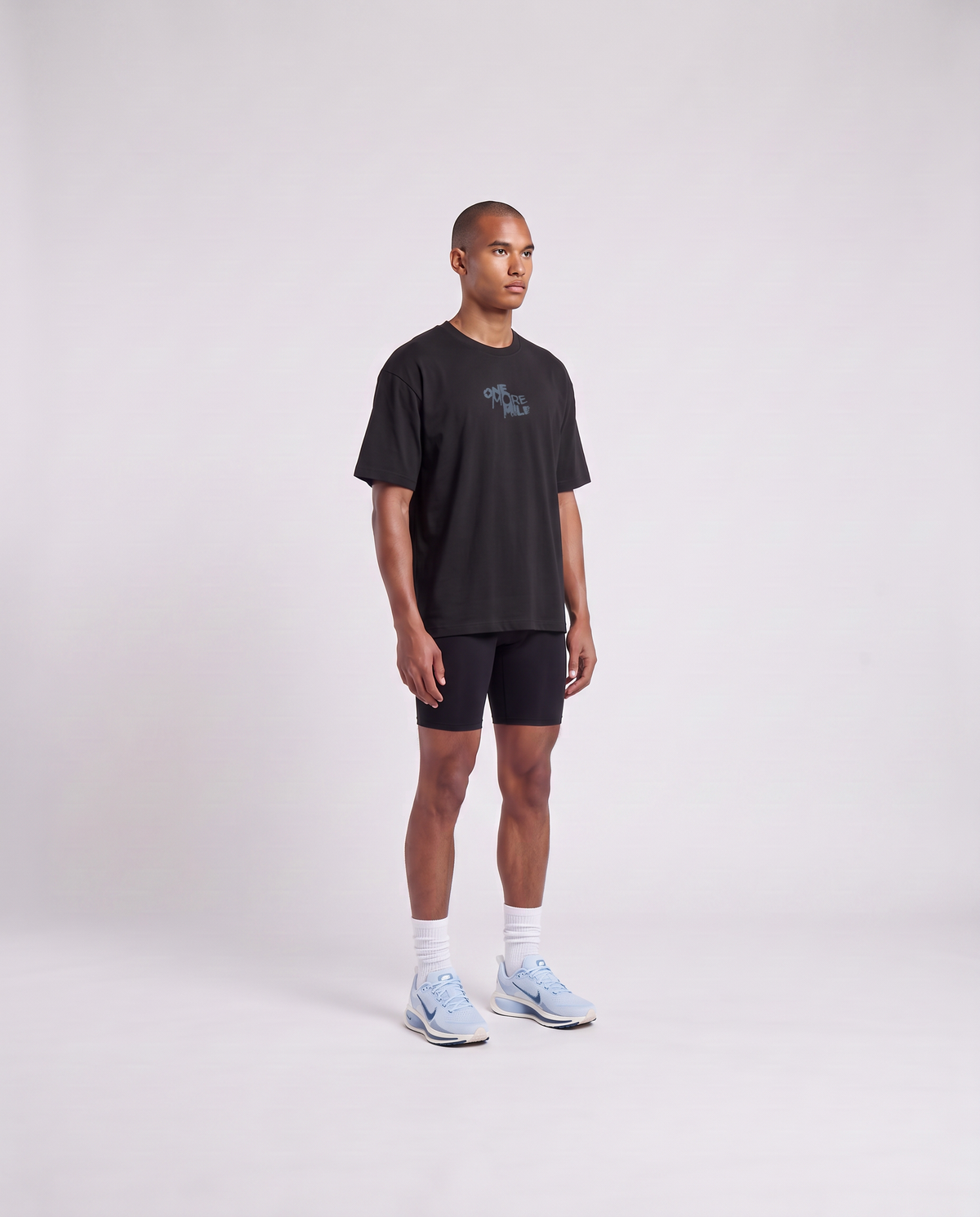 Model wearing the One More Mile oversize t-shirt in black — three-quarter view showing the oversize fit — Vista 3
