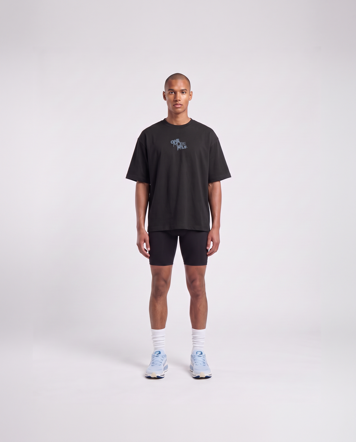 Model wearing the One More Mile oversize t-shirt in black — front view with the ONE MORE MILE graffiti mark at the chest in slate blue — Vista 2
