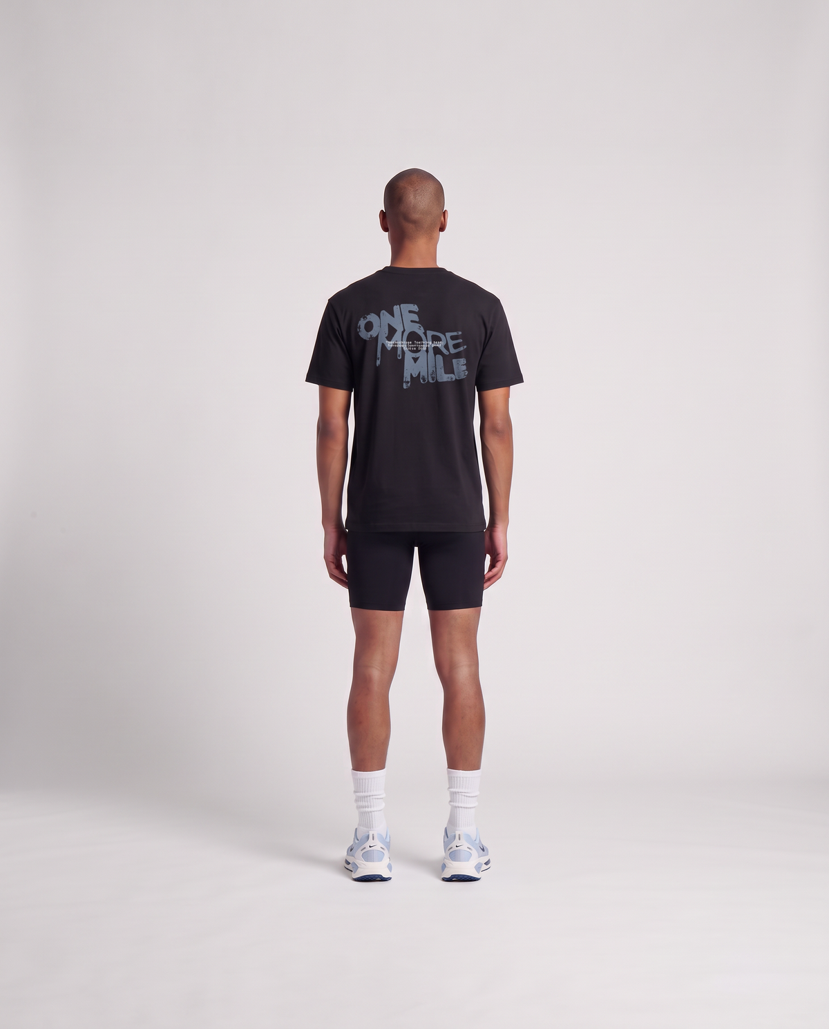 Model wearing the One More Mile t-shirt in black — back view with the dripping ONE MORE MILE graffiti print in slate blue