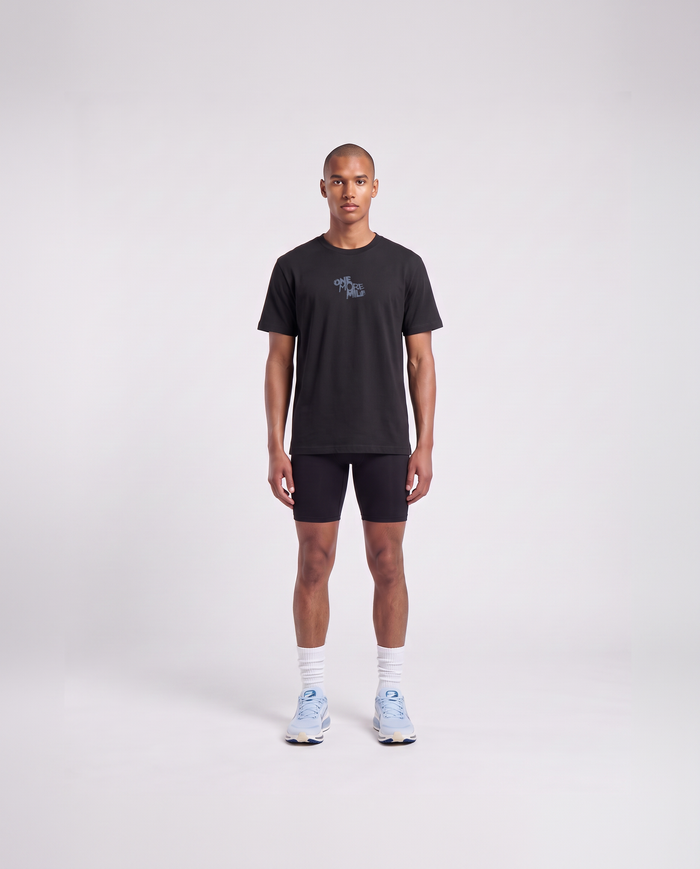 Model wearing the One More Mile t-shirt in black — front view with the ONE MORE MILE graffiti mark at the chest in slate blue