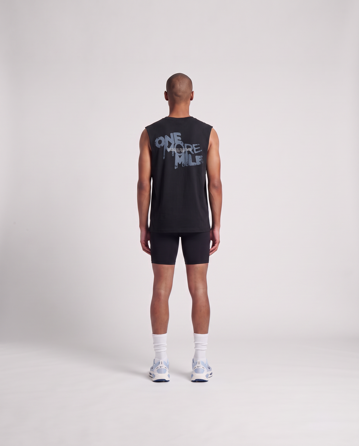 Model wearing the One More Mile tank top in black — back view with the dripping ONE MORE MILE graffiti print in slate blue