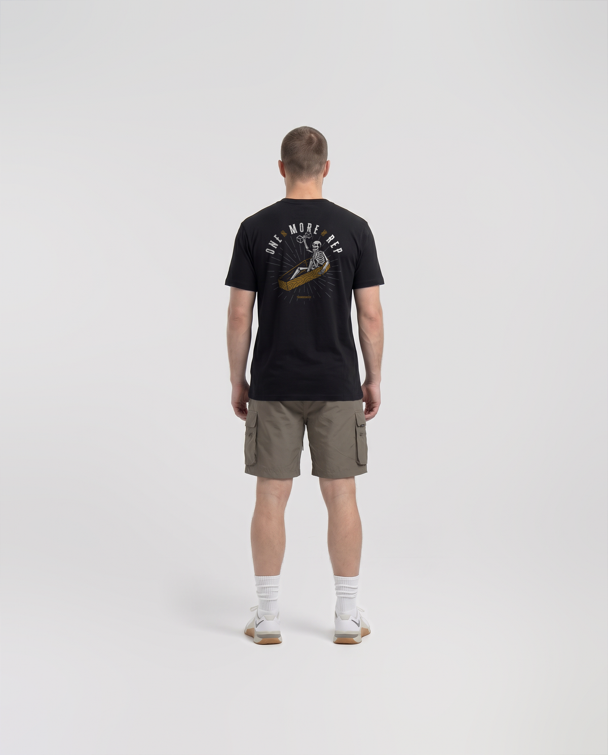 Model wearing the One More Rep t-shirt in black — back view with the skeleton pressing one last dumbbell out of an open coffin under ONE MORE REP in bone white and gold — Ansicht 4
